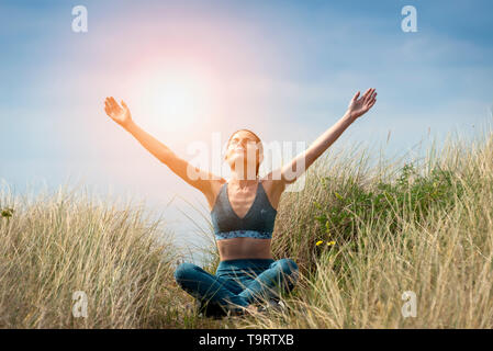 sporty woman sitting in lotus position with her arms raised to the sky and eyes closed meditating. Stock Photo