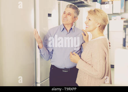 Mature married couple chooses refrigerator for their house in shop Stock Photo