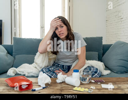 Sick woman in pain with headache migraine and temperature feeling ill with cold flu sitting on sofa at home. Lifestyle portrait . Health care, virus,  Stock Photo