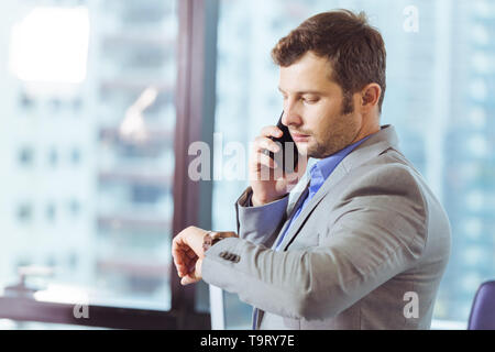 Business man looking at his watch while calling to partner in office, business time concept. Stock Photo