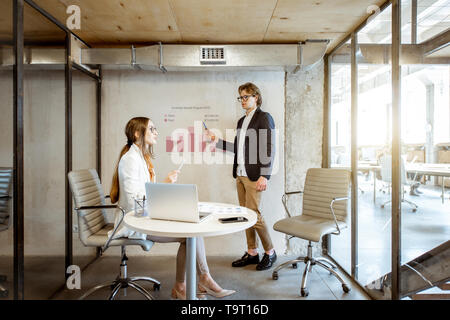 Man showing chart to his female business partner during the small conference in the meeting room Stock Photo