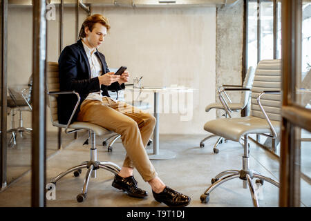 Young businessman sitting with smartphone during the coffee break in the meeting room Stock Photo