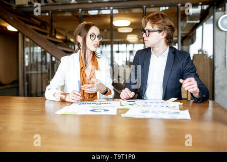 Business man and woman working with documents while sitting together at the wooden table in the office or coworking space Stock Photo