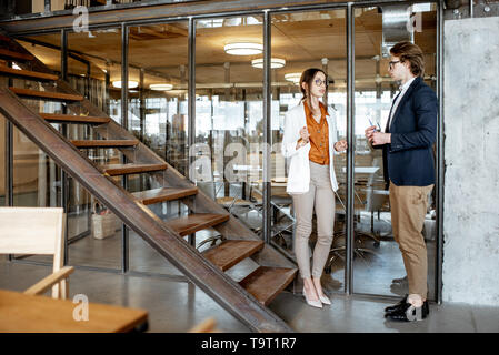 Young buiness man and woman having a conversation standing during the coffee break in the hall of the modern office Stock Photo