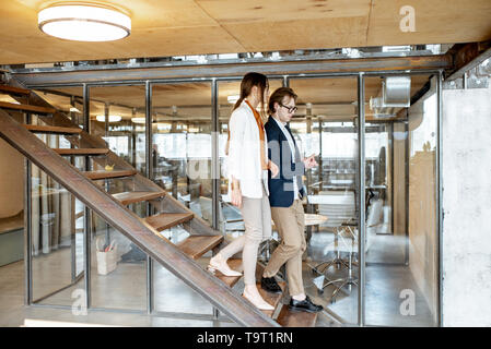 Business man and woman walking down the stairs in the hall of the modern office or coworking space Stock Photo