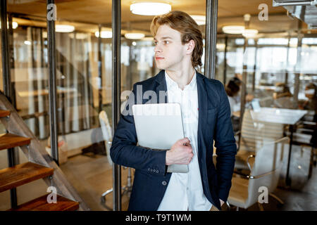 Portrait of a young and cherful business man standing with laptop in the office Stock Photo