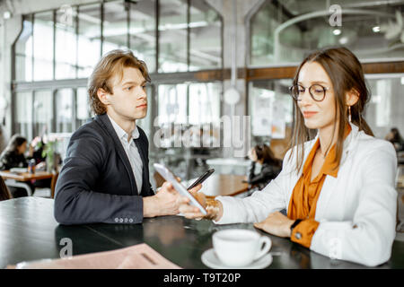 Young man and woman having business conversation while sitting together in the bar or coworking space Stock Photo