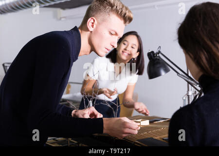 Student of faculty of architecture engaged in architectural modeling in studio with groupmates Stock Photo