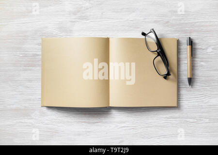 Opened book with blank craft paper pages, pen and glasses on light wooden background. Flat lay. Stock Photo