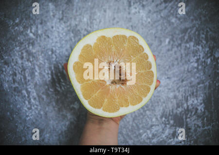 Tropical summery fruit called Pommelo looking fresh and juicy holding in hand on the gray and white background. Stock Photo