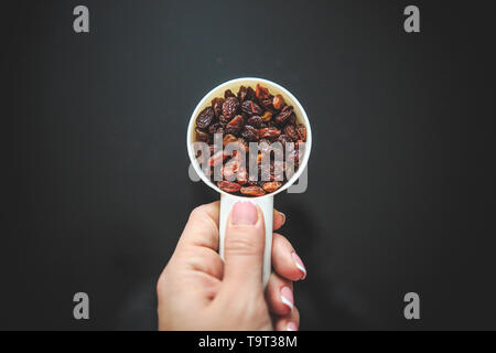 Raisins in the white measuring cup taken from the top on the back background. Stock Photo