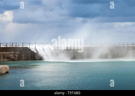 Coastal landscape with waves going over concrete breakwater under dark blue cloudy sky. Alexandria, Egypt Stock Photo
