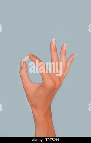 Beautiful female hand holds pill gesture. Isolated on blue background Stock Photo