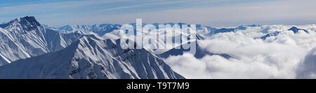 Panoramic view of snowy mountains covered with sunlit clouds at sunny winter day. Caucasus Mountains, Georgia, region Gudauri. Stock Photo