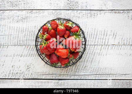 Ripe organic strawberry in vintage black metal vase on white wooden background. View from above. Stock Photo