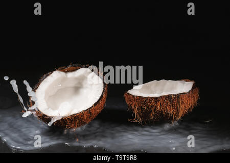 Ripe coconut and splash of milk on dark background Stock Photo