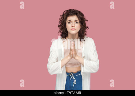 Please help me or give me one chance more. Portrait of hopeful young woman with curly hairstyle in casual style standing with palm hands and looking a Stock Photo