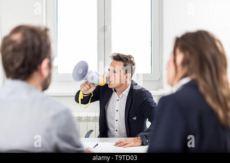 Businessman yelling at his colleagues by using megaphone on a meeting in the office. Stock Photo