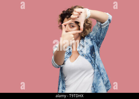 Portrait of serious attentive young woman with curly hairstyle in casual blue shirt standing with crop hands composition and looking at her target. in Stock Photo