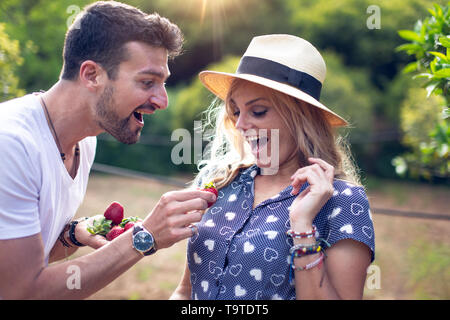 Spontaneous man giving strawberry to his surprised girlfriend, love and emotions Stock Photo