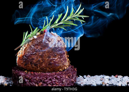 smoked veal loin with sesame and rosemary with rice and wine on a bed of salt and dark background Stock Photo