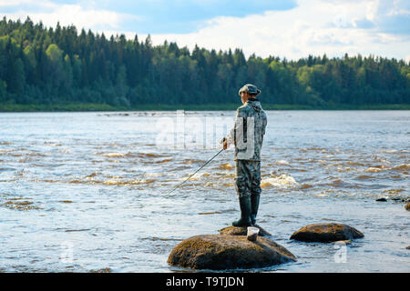 Man standing on a stone with fishing pole in the middle of a lake Stock  Photo - Alamy