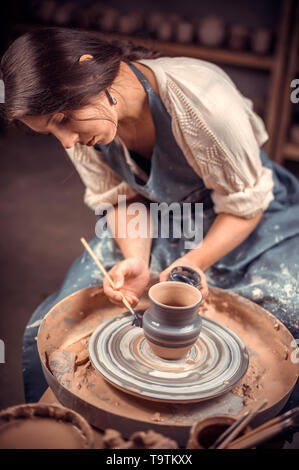 Charming young and cheerful woman demonstrates the process of making ceramic dishes using the old technology. Handmade products. Stock Photo