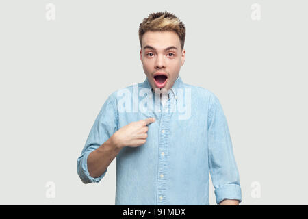 Who? me? Portrait of shocked handsome young man in light blue shirt standing, pointing himself and looking at camera with unbelievable face and asking Stock Photo