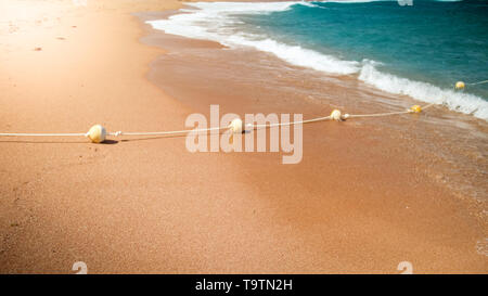 Closeup image of plastic floating buoys connected in line by rope lying on the sea beach. Perfect shot to illustrate summer holiday vacation at ocean. Stock Photo