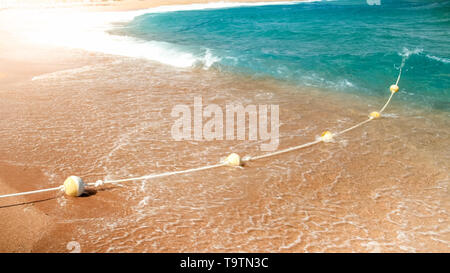 Closeup image of plastic floating buoys connected in line by rope lying on the sea beach. Perfect shot to illustrate summer holiday vacation at ocean. Stock Photo