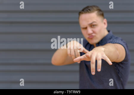 Laughing playful young man gesturing with his hands pointing at the camera with selective focus to his hand Stock Photo