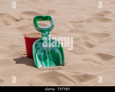 A red bucket and green spade on a warm soft sunny sandy beach. Taken at Oxwich Bay, Gower, Wales, UK. Stock Photo