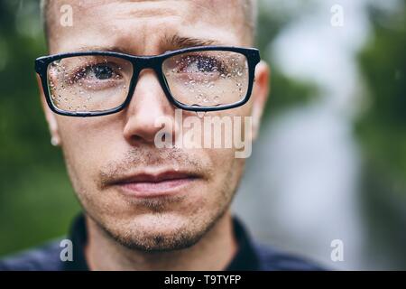 Portrait of young man with eyeglasses in rain. Selective focus on raindrops. Stock Photo
