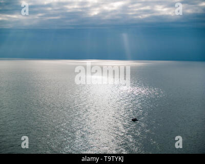 A small boat out on the sea, viewed from the coastal path, Gower. Overlooking the Bristol channel with beams of sunlight shining through the clouds. Stock Photo