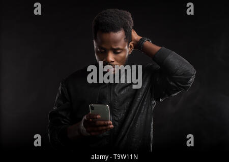 Indoor shot of impressed and amazed attractive African American man with beard and short haircut, holding smartphone, looking surprised at gadget scre Stock Photo