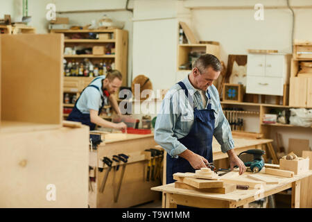 Portrait of two carpenters working with wood white assembling furniture in workshop, copy space Stock Photo