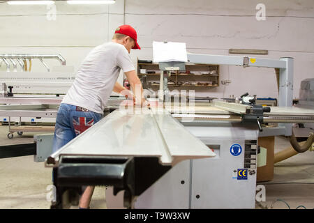 A male engineer controls the work of the machine in the furniture shop. Stock Photo