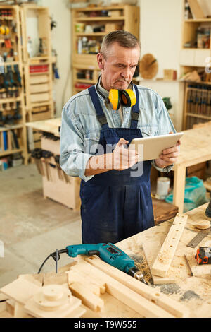 Portrait of modern senior carpenter using digital tablet while working in joinery Stock Photo