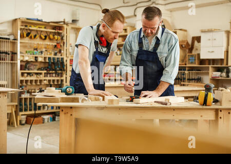 Portrait of senior carpenter teaching apprentice  standing at table in workshop, copy space Stock Photo