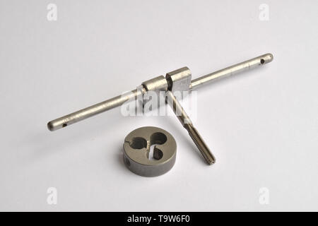 A metal thread cutting tap held in an apprentice hand made Tap Holder, with a thread cutting die beside it. Stock Photo