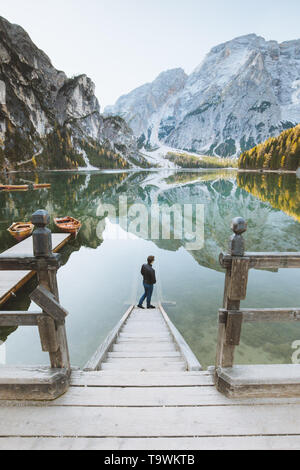 Beautiful view of a young man standing on wooden stairs watching the sunrise at famous Lago di Braies the Dolomites, South Tyrol, Italy Stock Photo