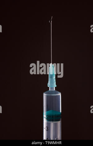 The end of the syringe with a needle filled with liquid on a dark background. Stock Photo