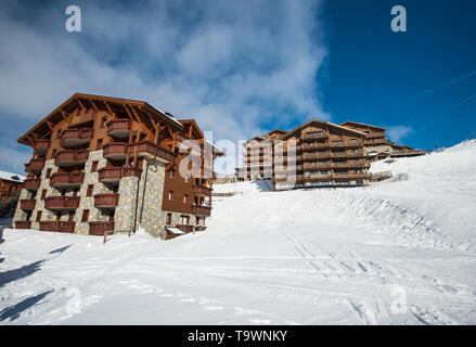 Panoramic view of snow covered piste in an alpine ski resort with apartment buildings on slope Stock Photo