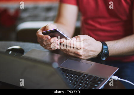 Man using smartphone working on laptop sitting at a desk Stock Photo