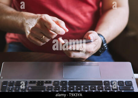 Man using smartphone working on laptop sitting at a desk Stock Photo
