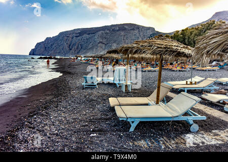 Oia, Santorini / Greece - 09.05.2018: Sunbeds at Kamari beach Santorini with a big rock in the background Stock Photo