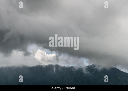 Bali, Indonesia - February 25, 2019: Rainy cloudscape over dark forested mountains in Bedougoel. Shades of gray. Stock Photo