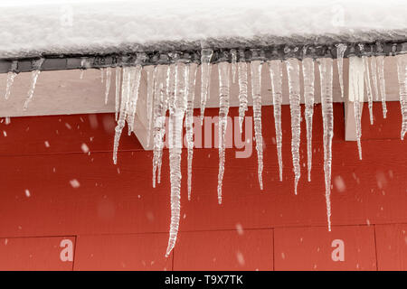 Icicles hanging from the roof against a red background. Stock Photo