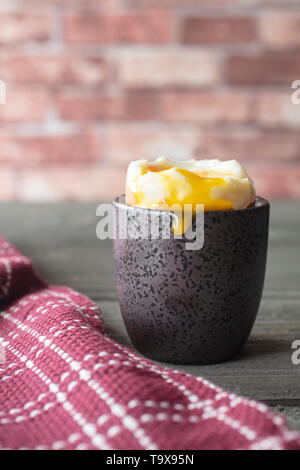 Soft boiled egg with cracked shell in a cup with yolk spilling over, next to a red dish towel on a vintage table Stock Photo