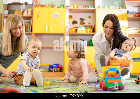 Nursery children playing with teacher and helper in kindergarten Stock Photo